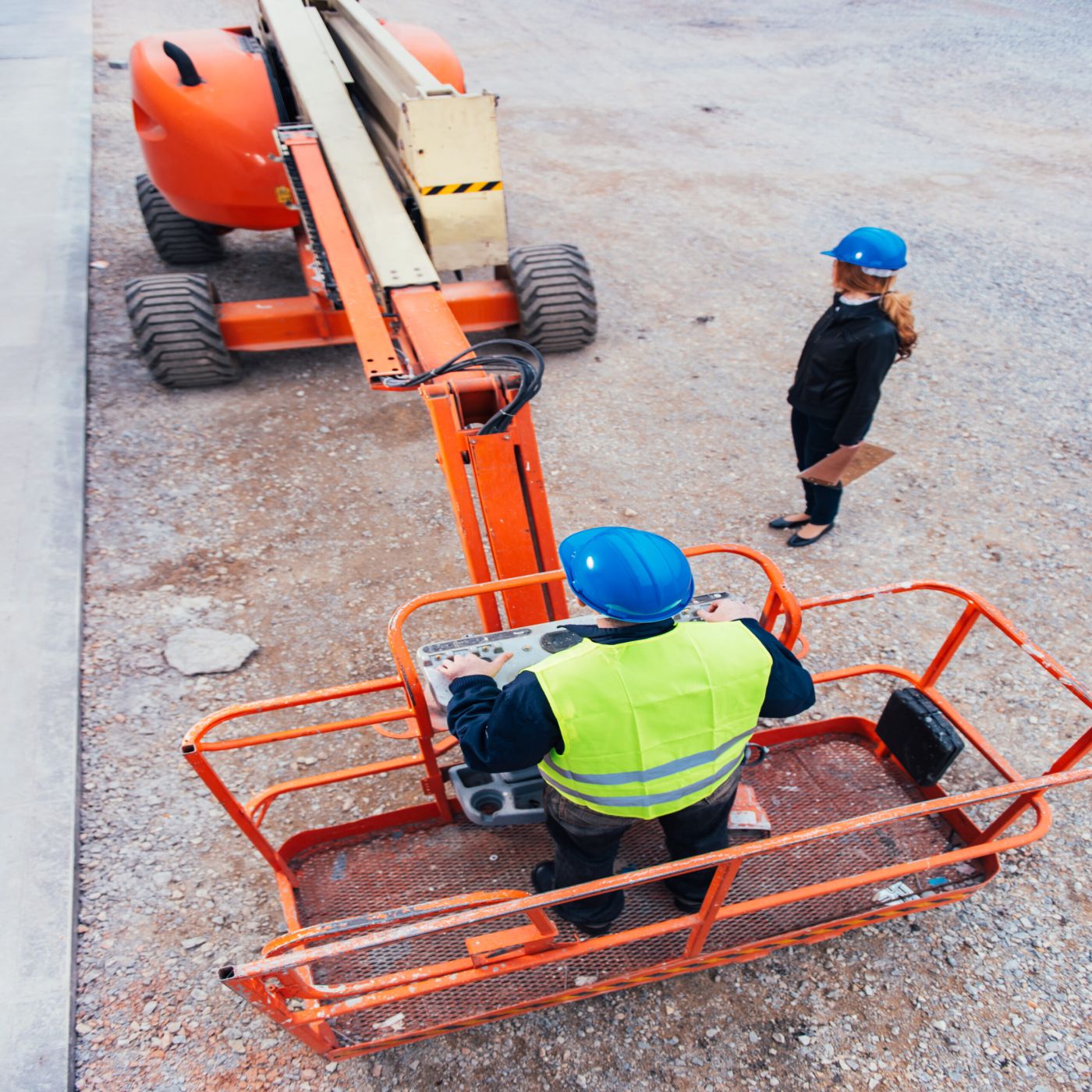 Boom lift operator at the platform controls with a supervisor on the ground