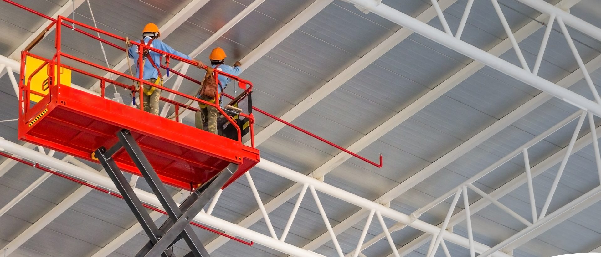 Two workers on a scissor lift inside a warehouse